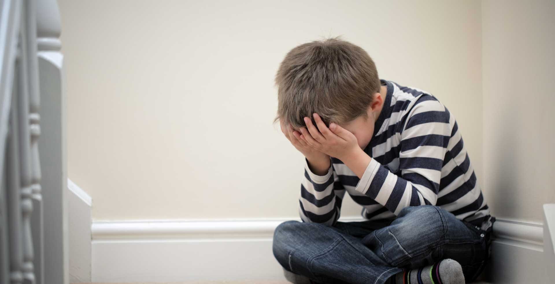 A child with his head in his hands as he sits on the floor