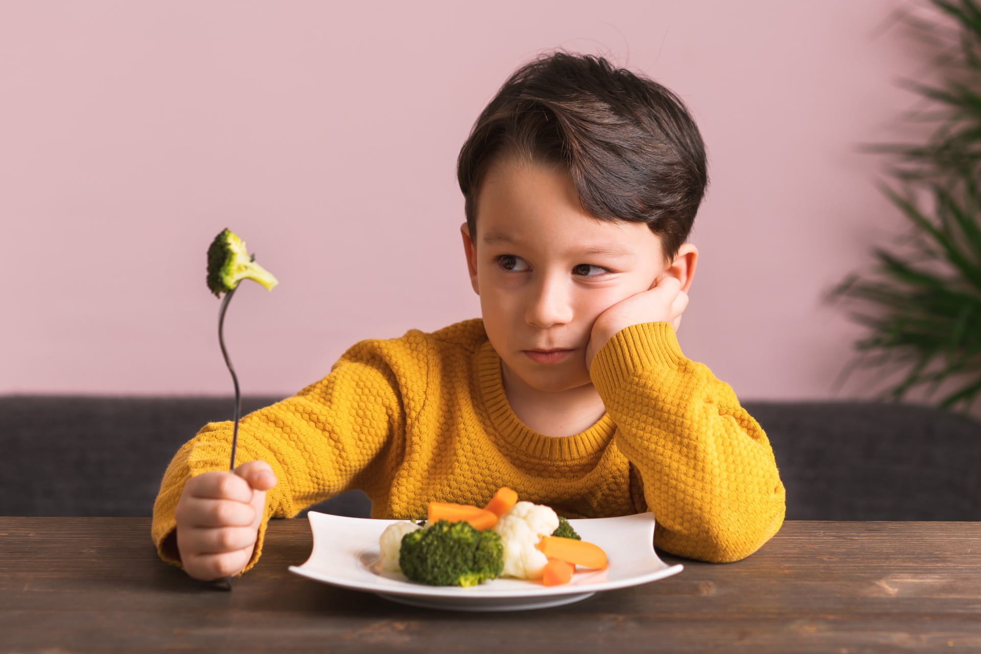A boy is very unhappy with having to eat vegetables. There is a lot of vegetables on his plate.