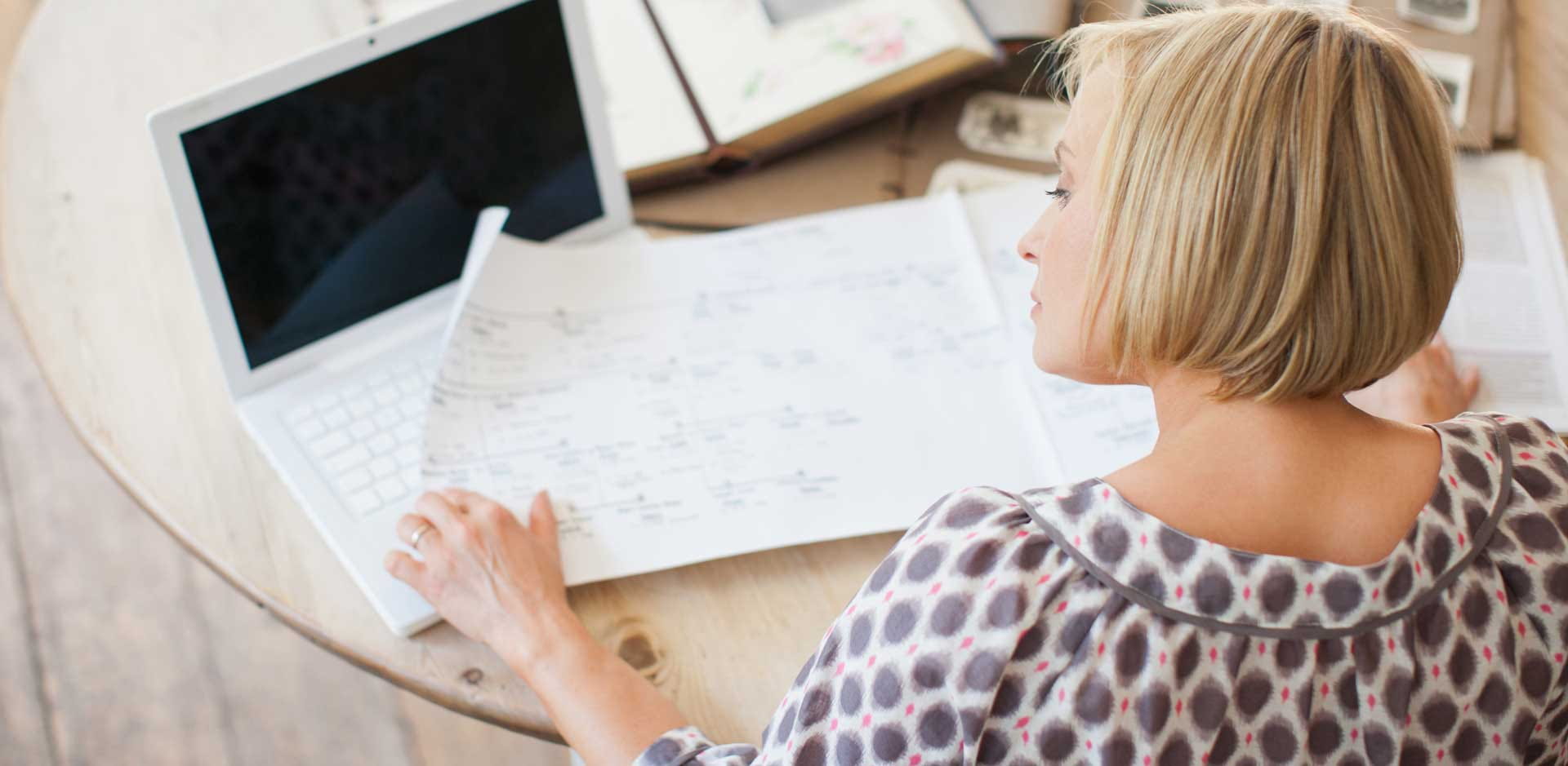 A lady is sitting at a table, looking at a family tree, with photo albums on the table alongside.