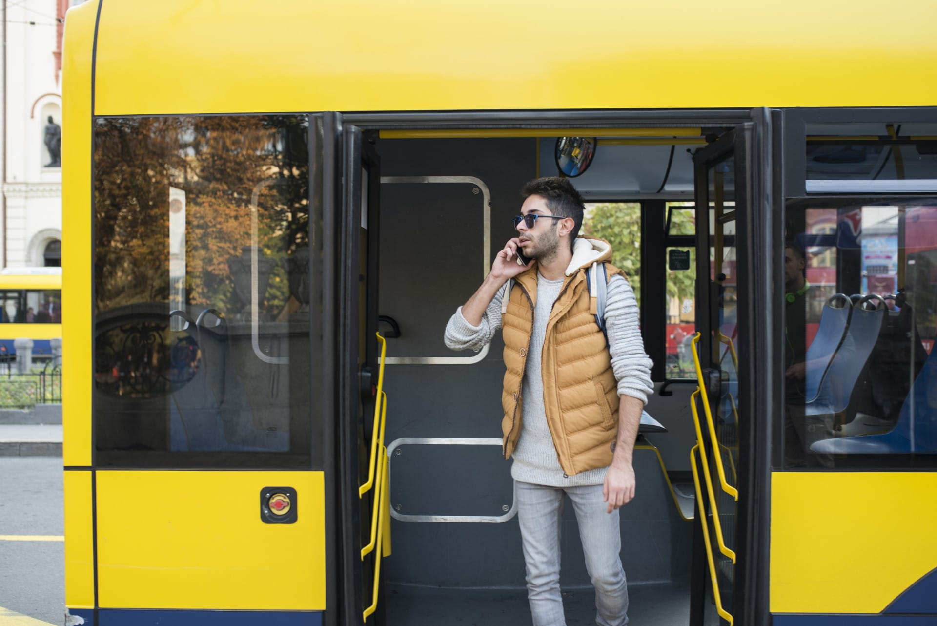 Young man exiting the bus and talking on his mobile phone